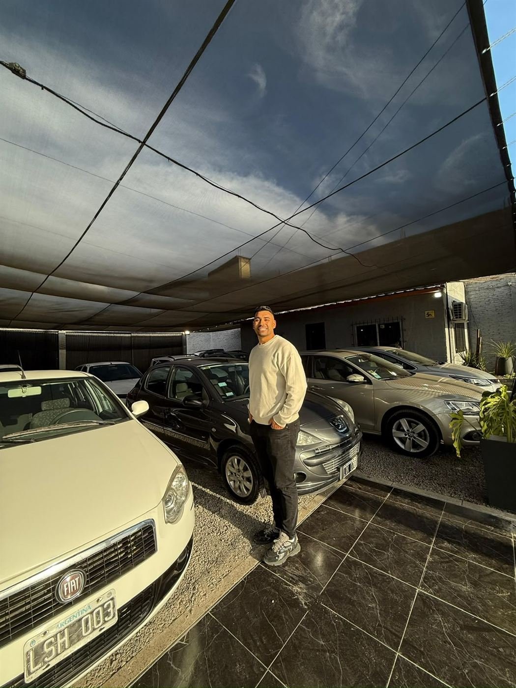 Nacho parado entre autos dentro de la agencia