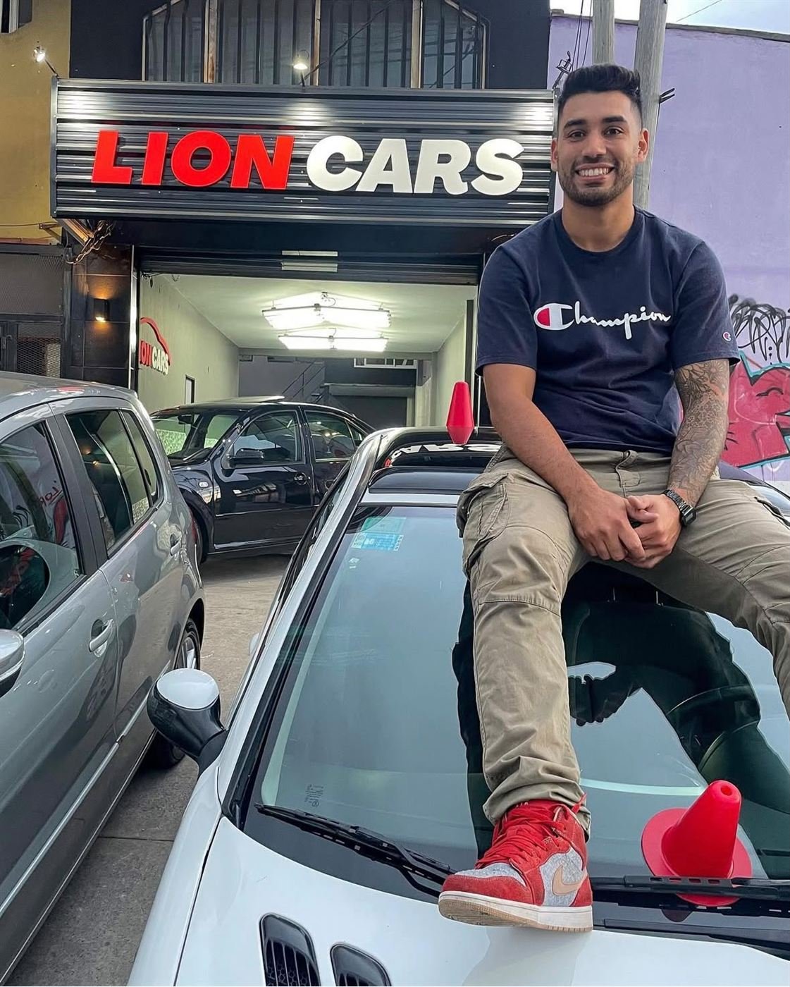 Nacho sentado sobre un auto frente al cartel de Lion Cars